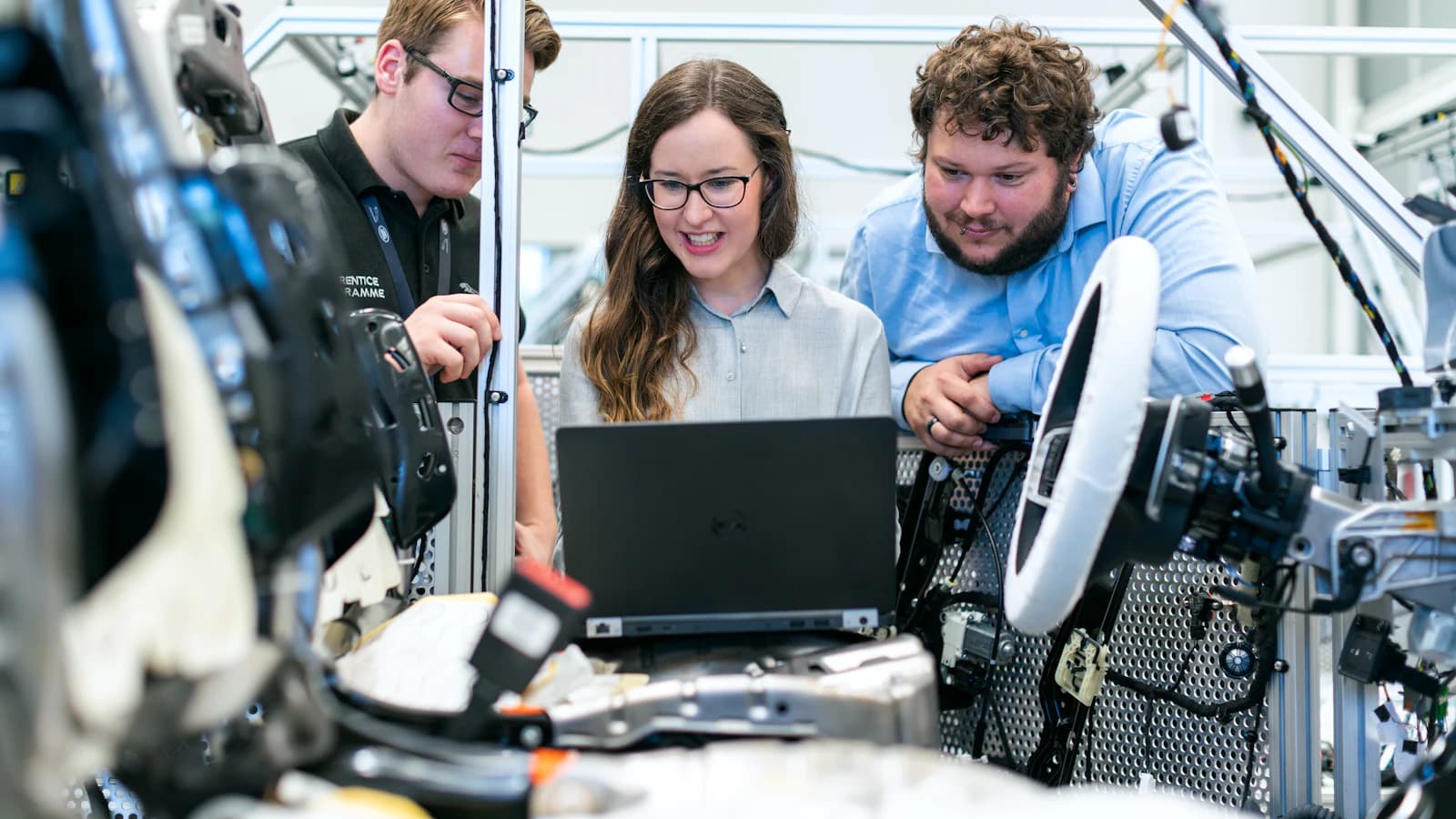 Engineers reviewing test data on a laptop next to a wiring harness and robotics rig in a lab
